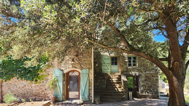 A rustic stone building with a wooden door and shutters, surrounded by trees and a gravel path. - Secluded vacation rental with a pool in the heart of the Corbières – Nature & Relaxation (Lairière)