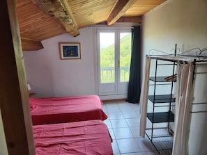 A room with a wooden ceiling, a bed with a pink bedspread, a window with a view of greenery, and a metal shelf unit. - Secluded vacation rental with a pool in the heart of the Corbières – Nature & Relaxation (Lairière)