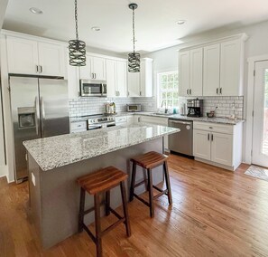 A modern kitchen with white cabinetry, stainless steel appliances, a granite countertop, and two wooden stools. - Rocky Branch Retreat (Belmont)