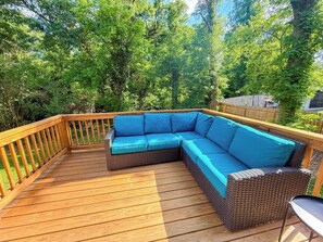 Eine Holzterrasse mit einem Rattansofa und einem kleinen Tisch.