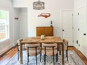 A dining area with a wooden table, four chairs, a decorative wall piece, and a hanging light fixture. - Rocky Branch Retreat (Belmont)