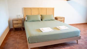 Habitación individual con una cabecera de mimbre, dos mesitas de noche y piso de baldosas.