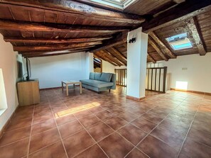 A spacious room with a high ceiling, a wooden beam structure, a sofa, a small table, and a television on a stand. - Casona del Tajuña (Armuña de Tajuña)
