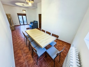 A dining area with a long wooden table surrounded by chairs, a sofa, and a radiator.