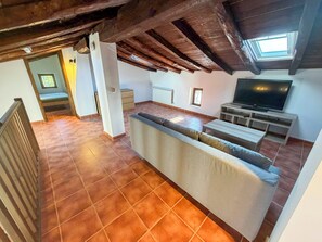 An open-plan living area with a kitchen, a sofa, a TV, and a staircase leading to an upper floor. - Casona del Tajuña (Armuña de Tajuña)