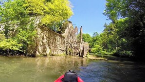 Ein Fluss mit einem roten Kajak im Vordergrund, umgeben von üppiger Vegetation und felsigen Klippen.
