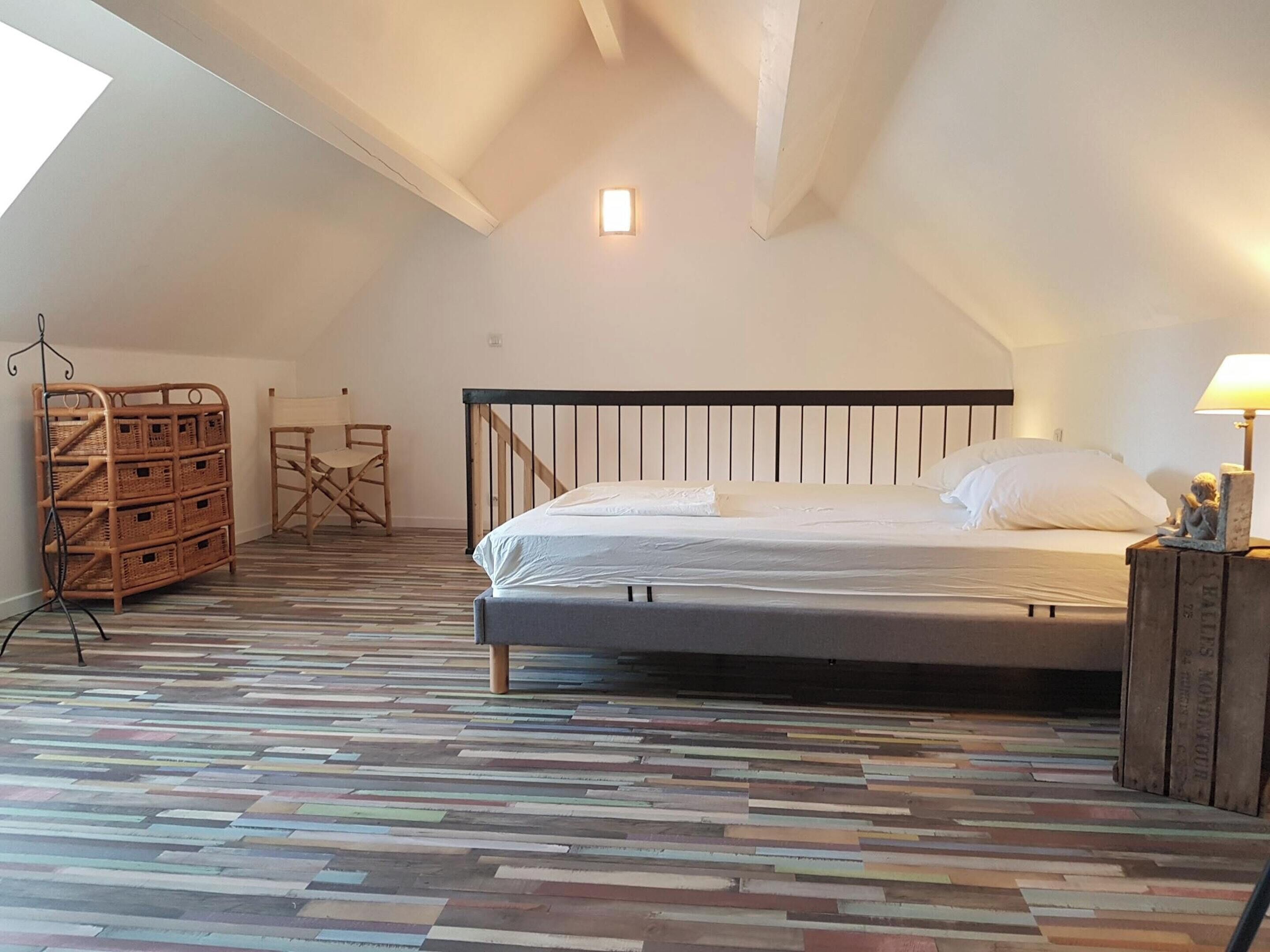 A bedroom with a bed, a wooden floor, a small table, and a chair.