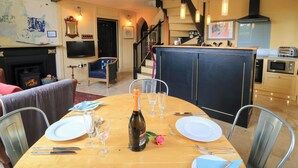 A dining area with a wooden table set for four, a fireplace, and a kitchen in the background. - The Sunday School Room (Sherborne)