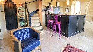 A modern interior with a bar area, a staircase, and a seating area with a blue chair. - The Sunday School Room (Sherborne)