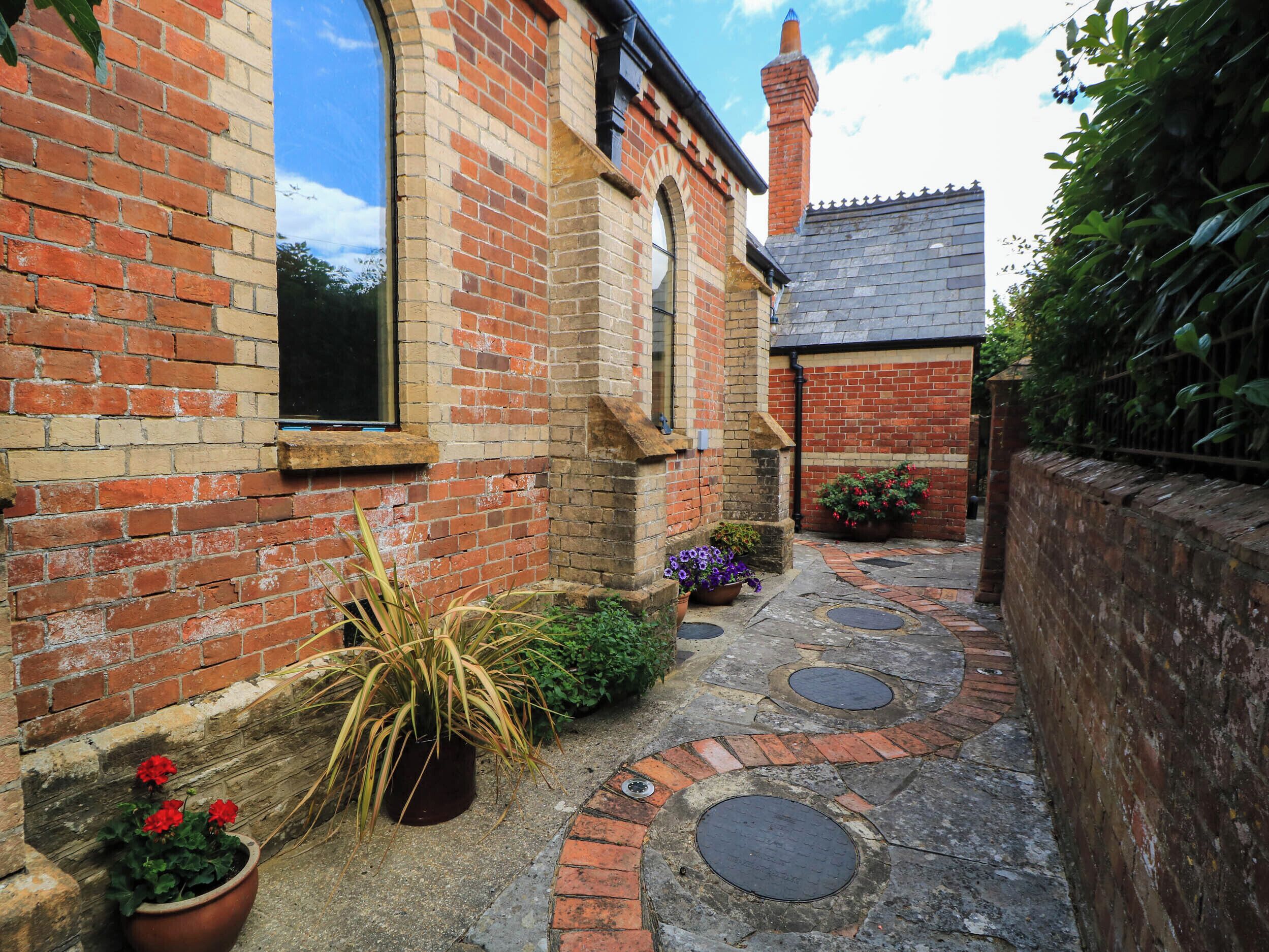 A narrow brick pathway leading to a building with a traditional design, including a chimney and a window with a black frame.
