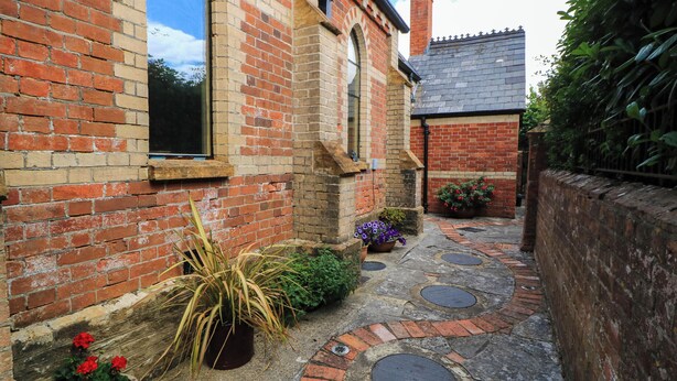 A narrow brick pathway leading to a building with a traditional design, including a chimney and a window with a black frame. - The Sunday School Room (Sherborne)