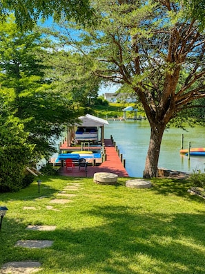A dock with boats, a covered seating area, and a tree-lined pathway leading to a body of water. - Cozy Creekside Cottage – AC, Dock, Kayaks & Firepit (Deltaville,)