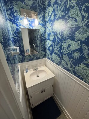 A bathroom with a white sink, a mirror, and a blue patterned wall. - Cozy Creekside Cottage – AC, Dock, Kayaks & Firepit (Deltaville,)
