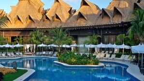 Ein Resort mit Swimmingpool, Liegestühlen und strohgedeckten Gebäuden.