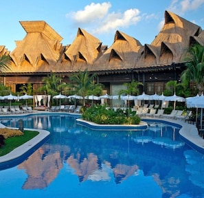 Ein Resort mit Swimmingpool, Liegestühlen und strohgedeckten Gebäuden.