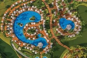 Ein Resort mit mehreren Schwimmbecken, Liegestühlen und Palmen.