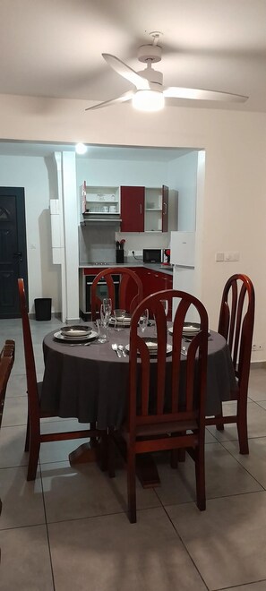 A dining area with a round table, four wooden chairs, and a ceiling fan.