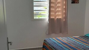 Un dormitorio con una cama, un ventanal con persianas, una puerta con unidad de aire acondicionado y un cuadro colgado en la pared.