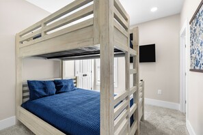 Ein Etagenbett mit blauer Decke und Kissen, ein Flachbildfernseher an der Wand und eine Tür mit floralem Vorhang.