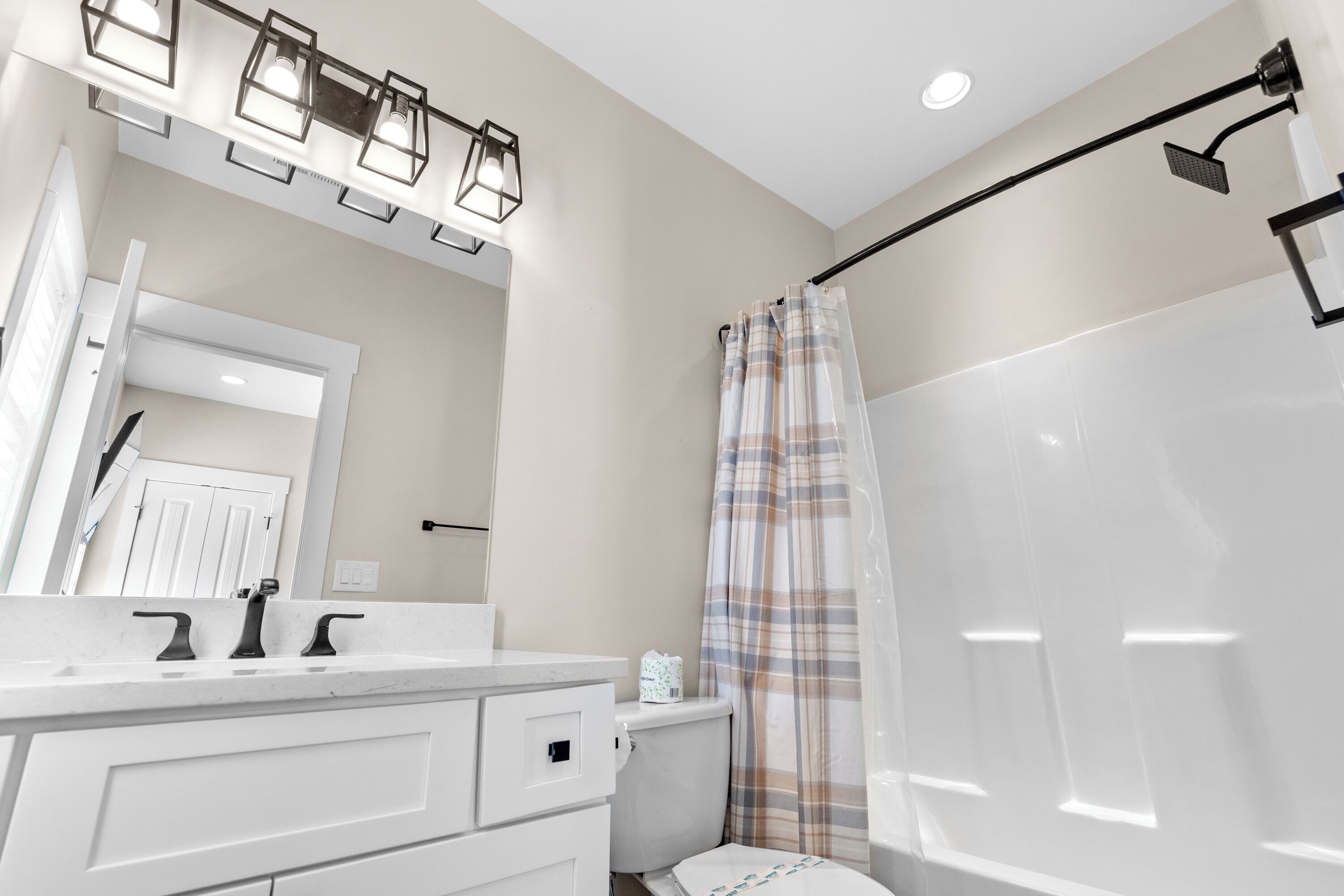 Een badkamer met een wit wastafelmeubel, toilet en douche met ruitjesgordijn, plus een plafondlamp.