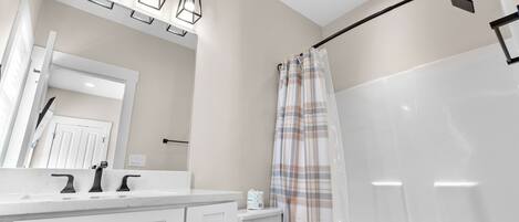 Een badkamer met een wit wastafelmeubel, toilet en douche met ruitjesgordijn, plus een plafondlamp.