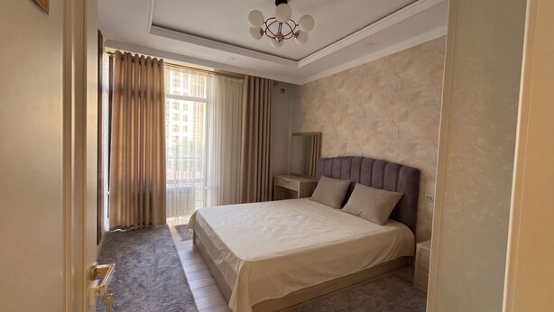 A hotel room with a large bed, a bedside table, a mirror, and a window with curtains. - Fabulous 2-bedroom apartment with AC in charming Toshkent (Тоshkent)
