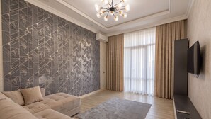 A modern living room with a sectional sofa, a patterned wall, a large window with curtains, and a mounted TV. - Fabulous 2-bedroom apartment with AC in charming Toshkent (Тоshkent)