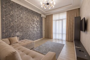 A modern living room with a sectional sofa, a patterned wall, a large window with curtains, and a mounted TV. - Fabulous 2-bedroom apartment with AC in charming Toshkent (Тоshkent)