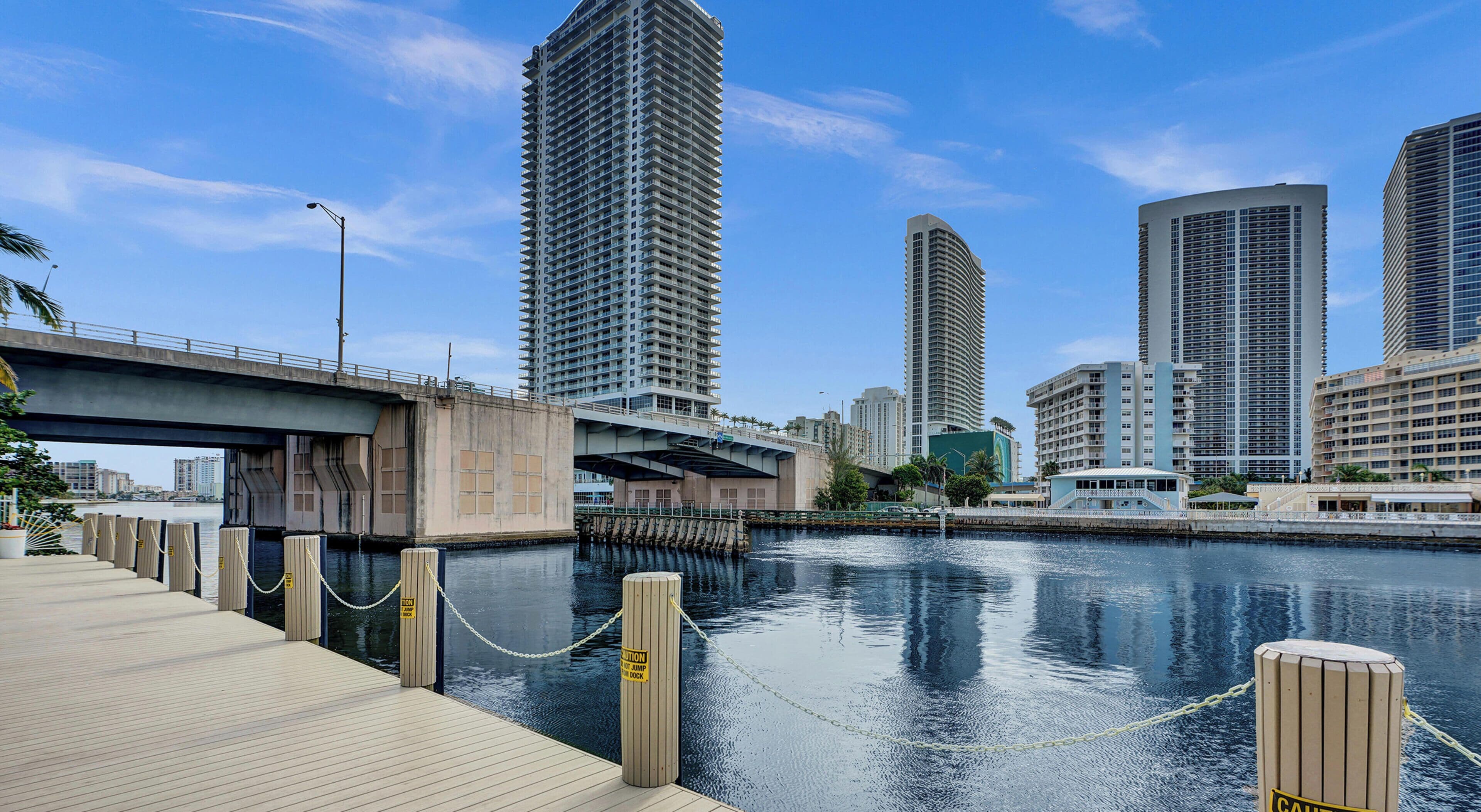 Vista al agua con muelle, un puente y edificios altos al fondo.