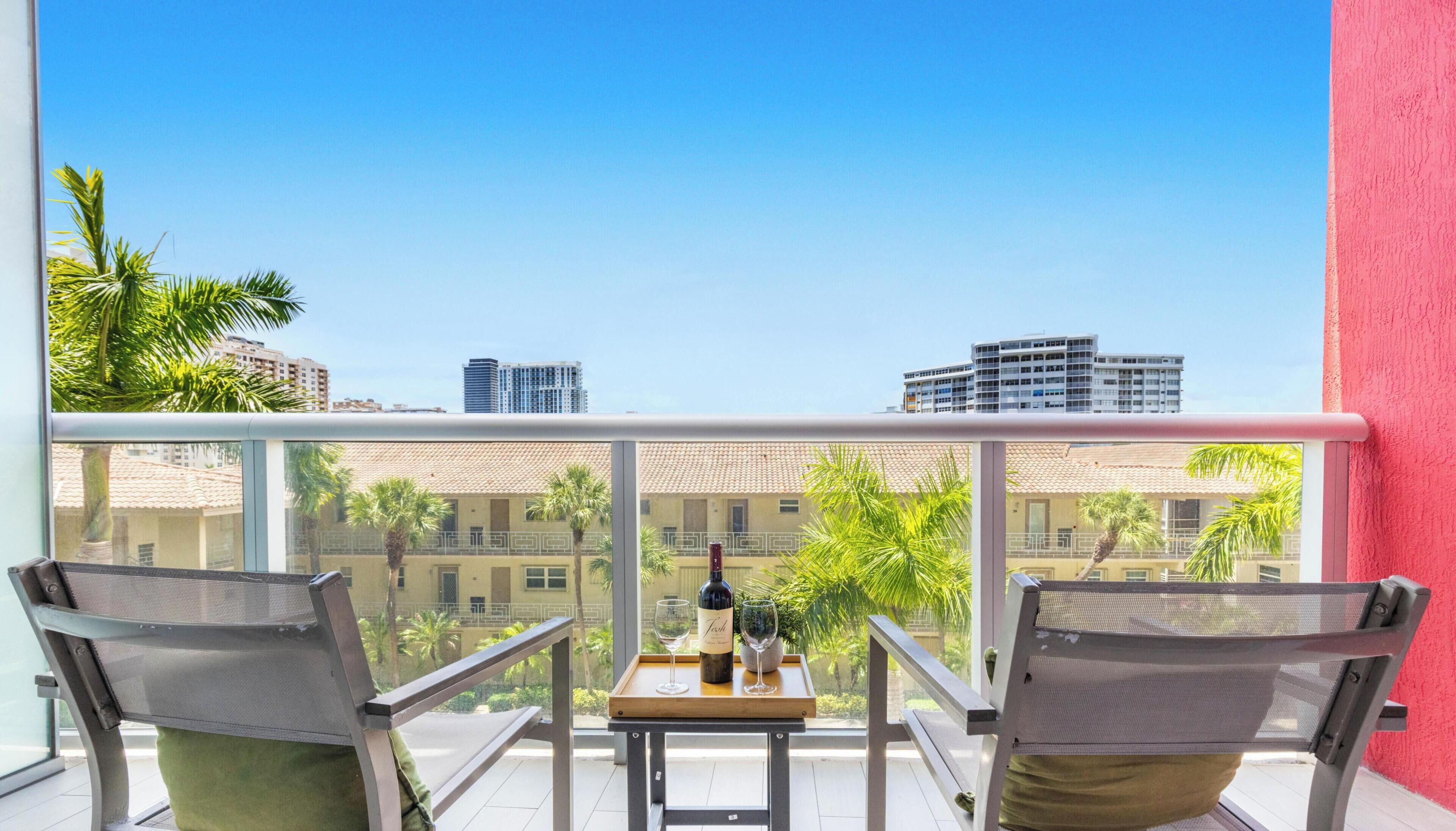 A balcony with two chairs, a table, and a bottle of wine.