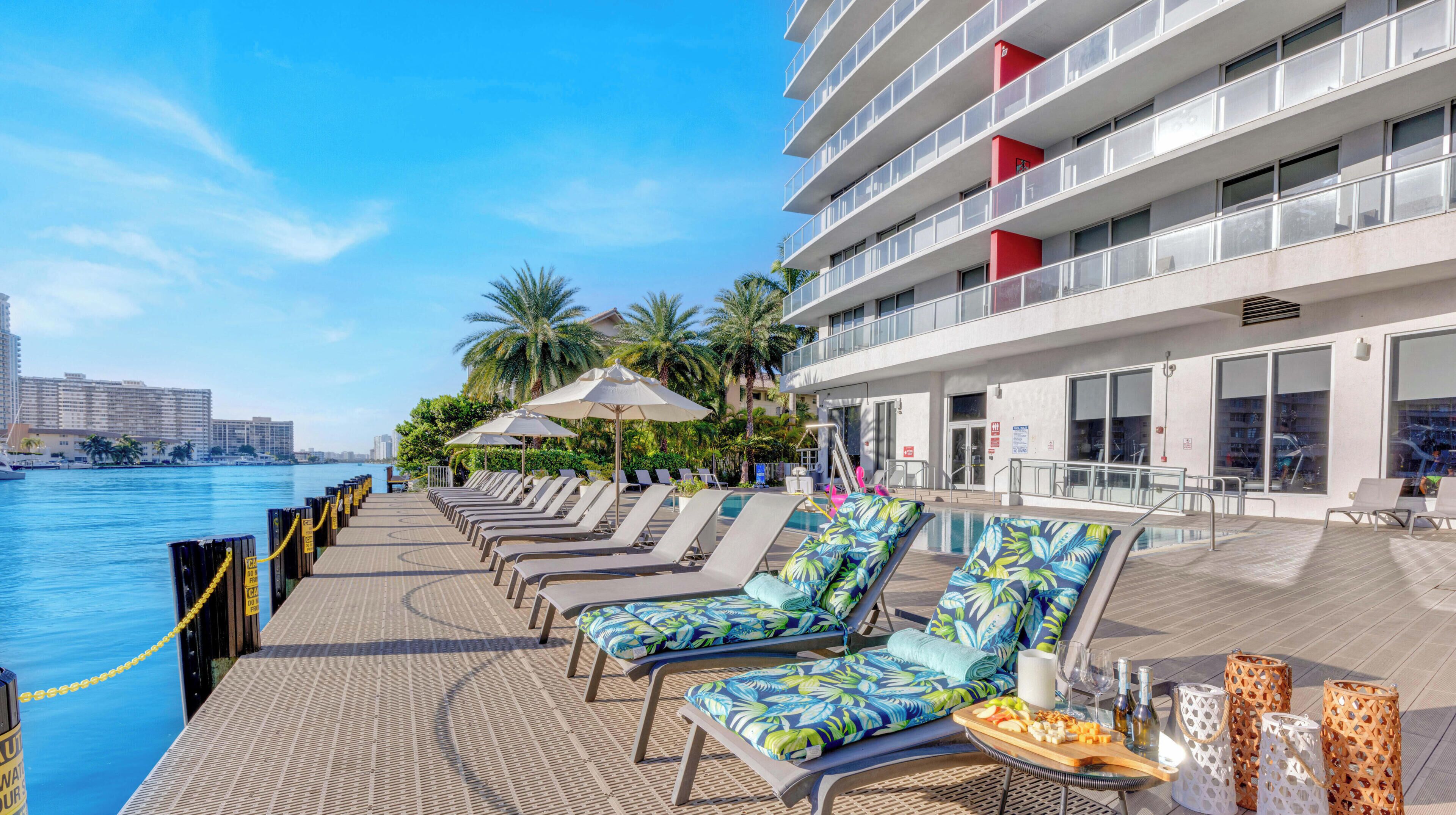 A poolside area with lounge chairs, umbrellas, and a view of the water.