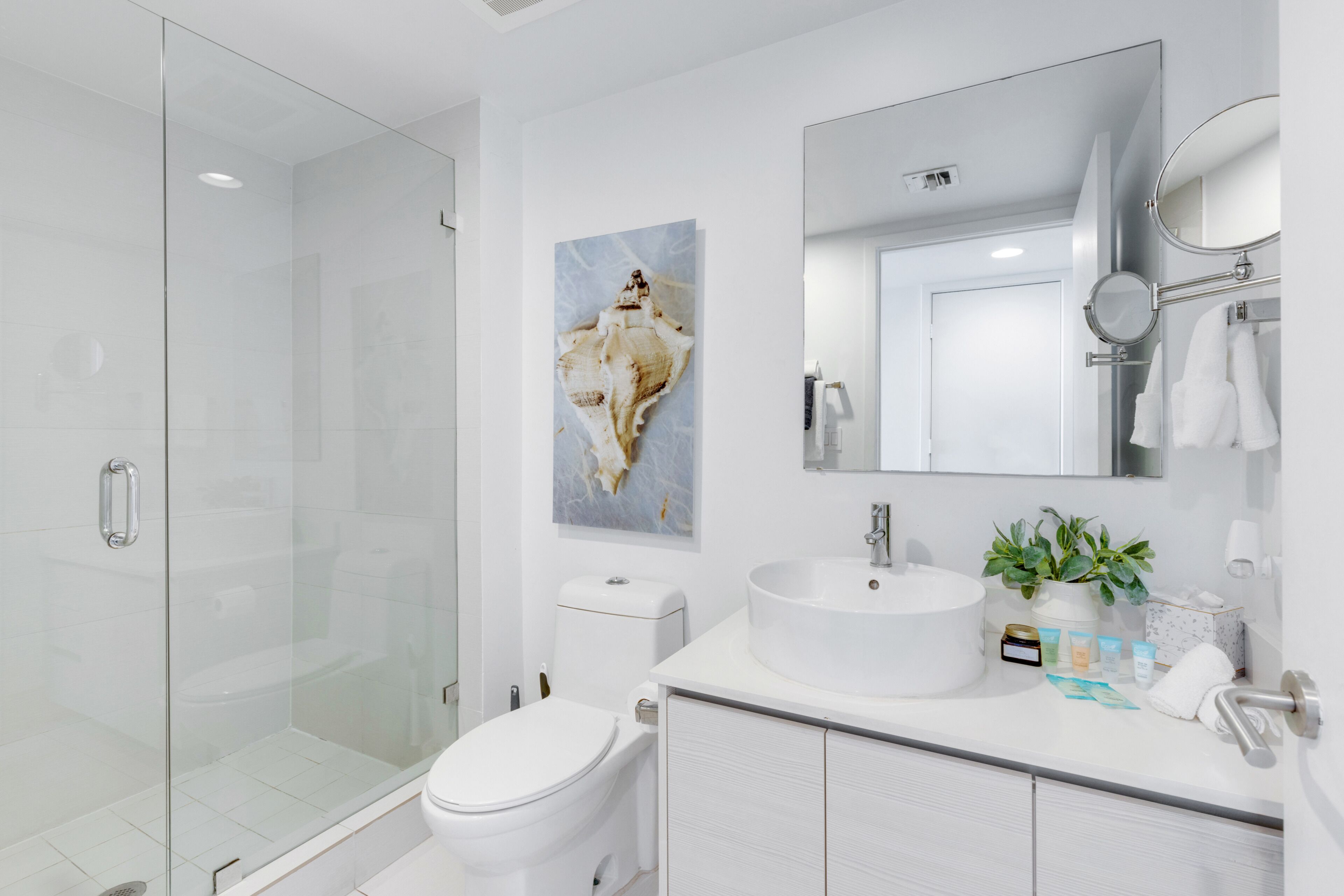 Une salle de bain moderne avec une douche à parois de verre, des toilettes blanches, un lavabo avec un miroir au-dessus et un porte-serviettes fixé au mur.