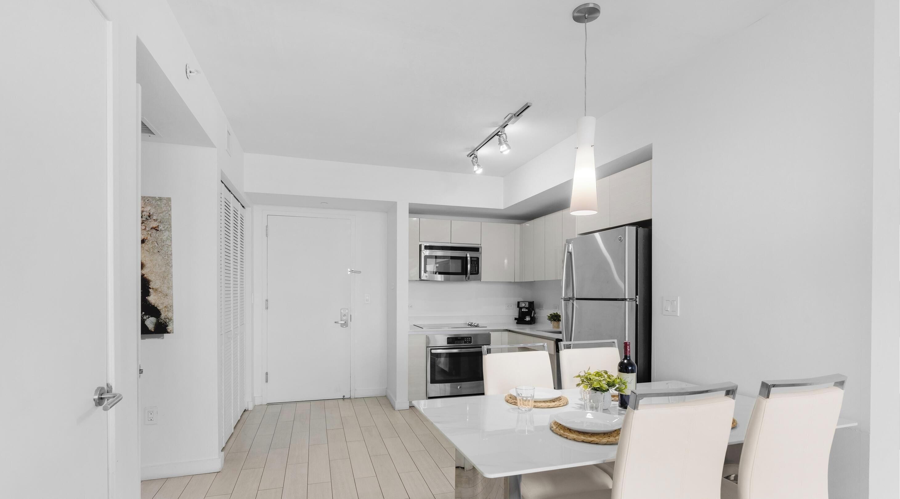 Una cocina moderna con armarios blancos, electrodomésticos de acero inoxidable y un comedor con mesa y sillas blancas.