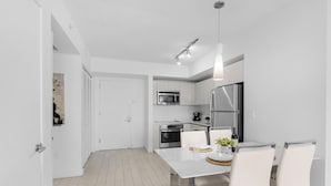 A modern kitchen with white cabinetry, stainless steel appliances, and a dining area with a white table and chairs.