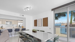 Une cuisine moderne avec un coin repas, une grande fenêtre donnant sur des palmiers et un luminaire au plafond.