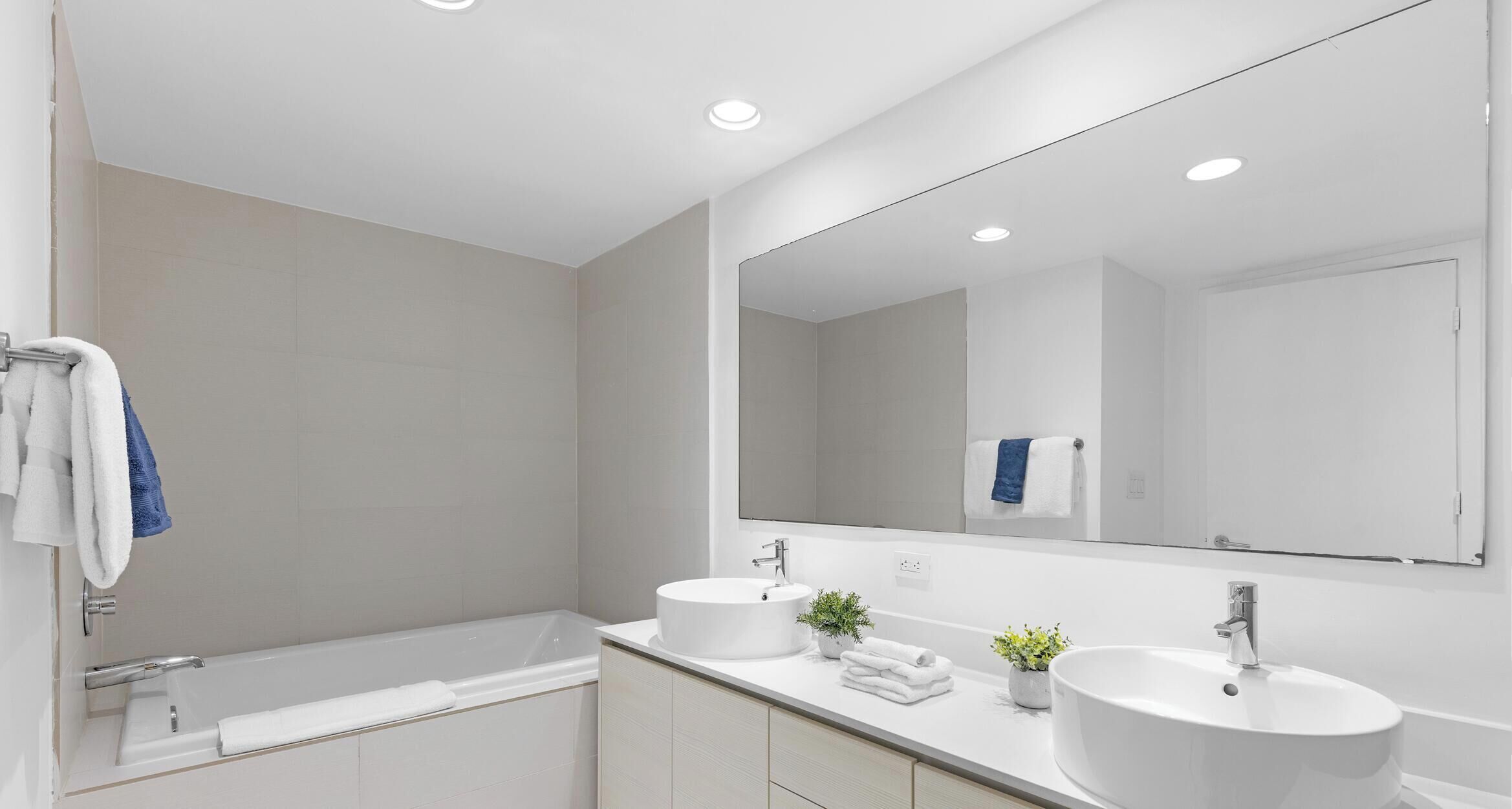 A modern bathroom with a bathtub, two sinks, and a large mirror.