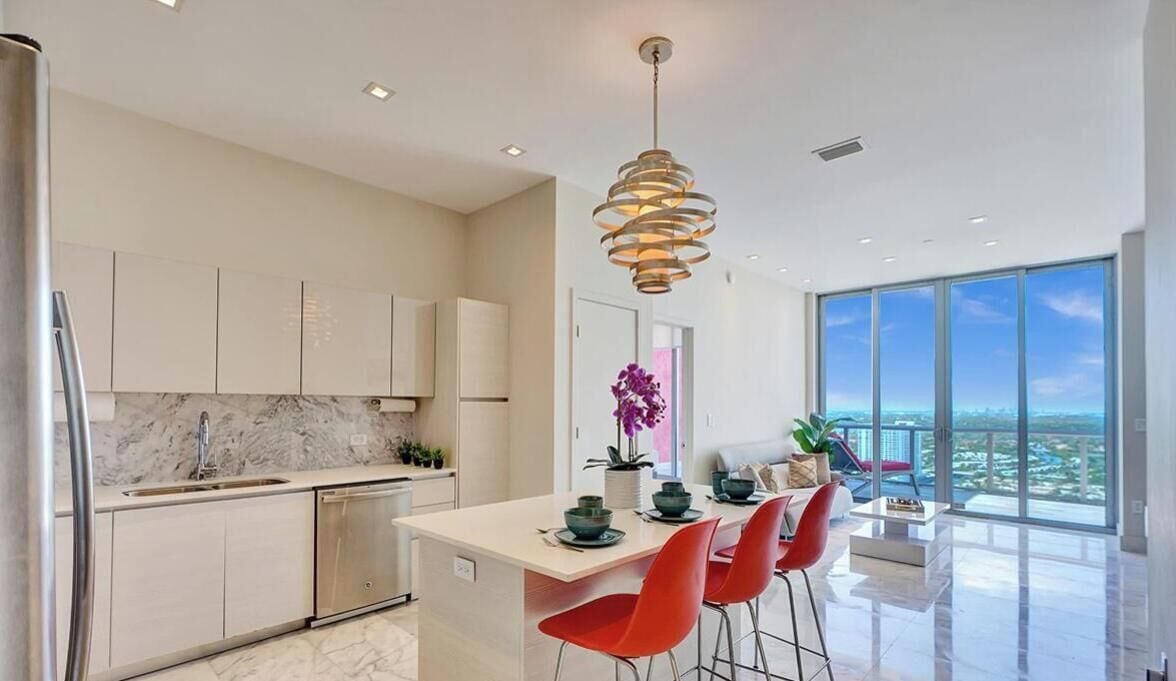 A modern kitchen with a marble countertop, stainless steel appliances, and a dining area with red chairs.
