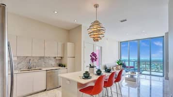 Una cocina moderna con encimera de mármol, electrodomésticos de acero inoxidable y una zona de comedor con sillas rojas.