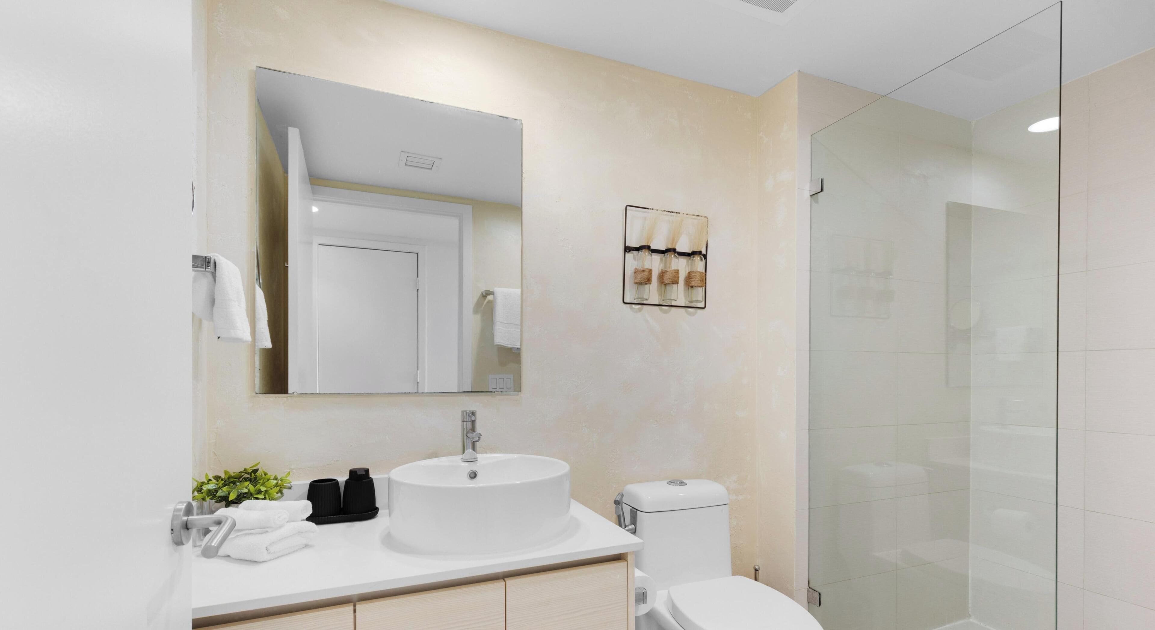Et moderne badeværelse med en hvid vask, toilet og en brusekabine med glas.
