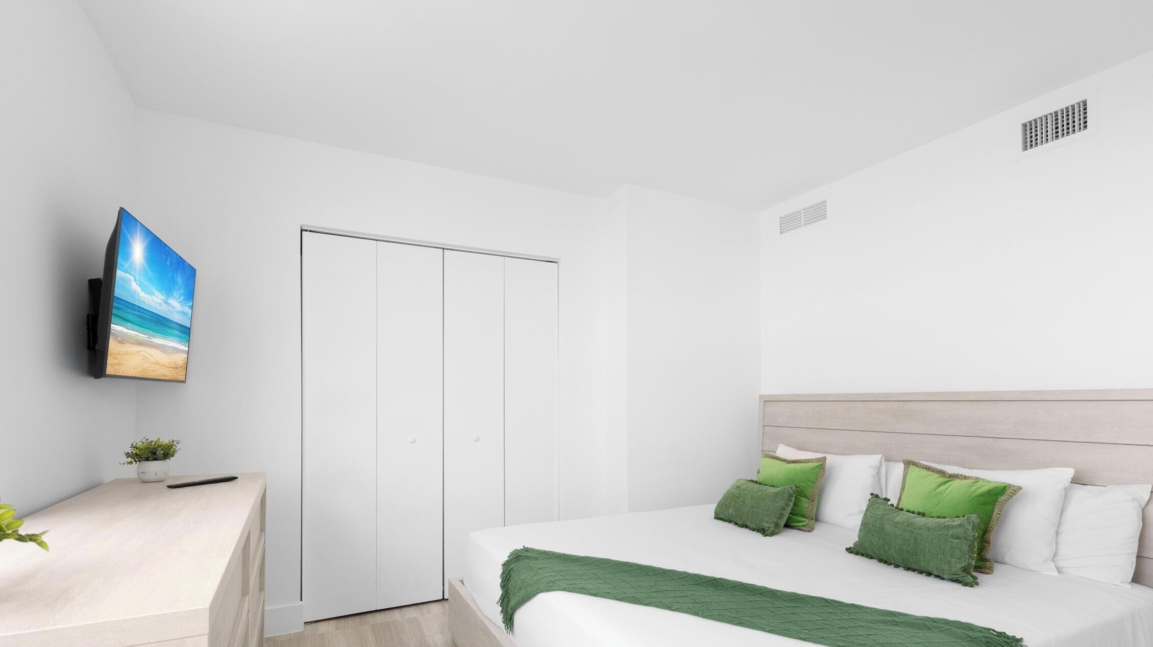 Ein modernes Schlafzimmer mit einem Bett, einem an der Wand befestigten Fernseher und einem weißen Kleiderschrank.