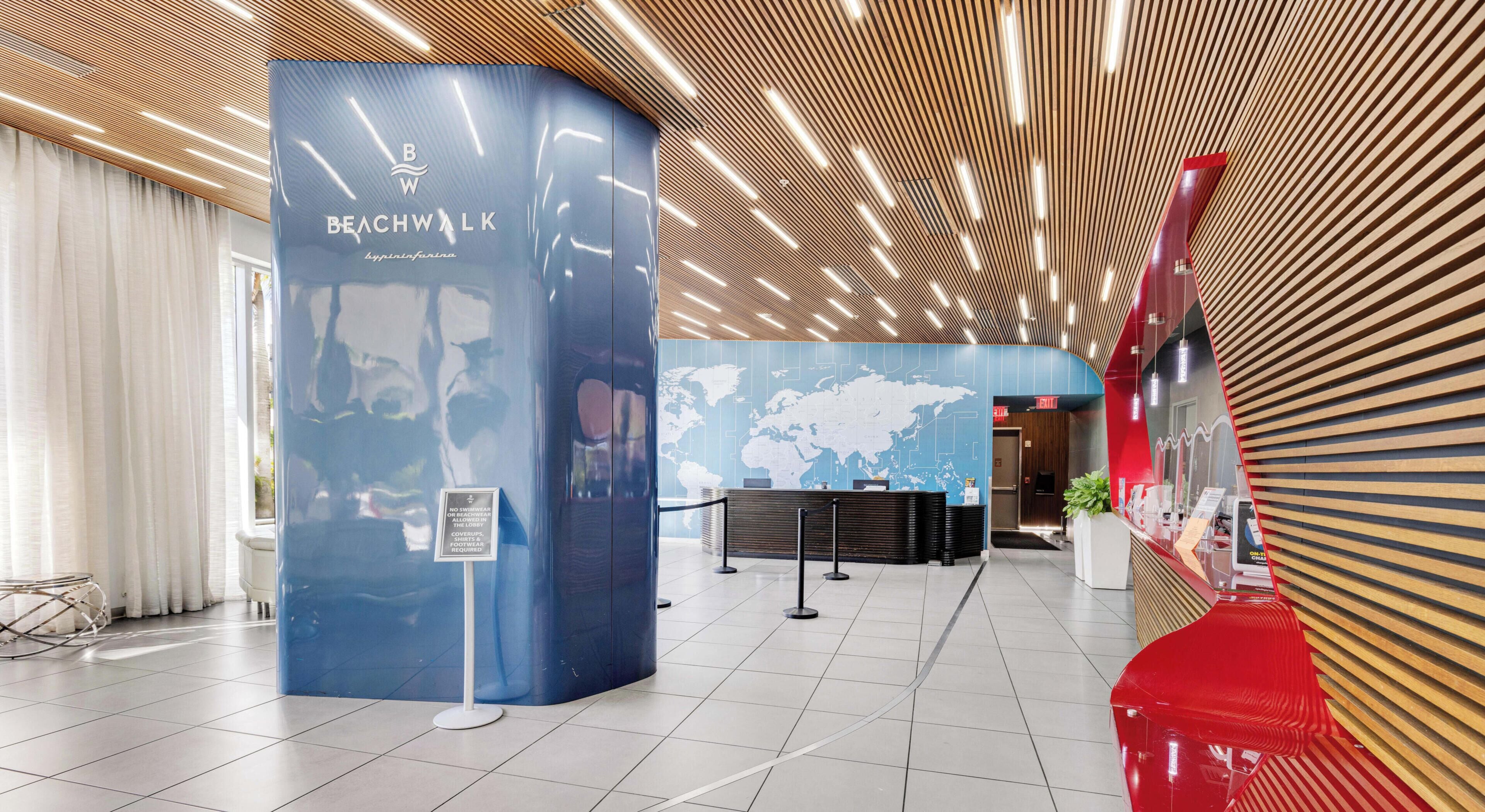 A modern lobby with a reception desk, a world map on the wall, and a wooden ceiling design.