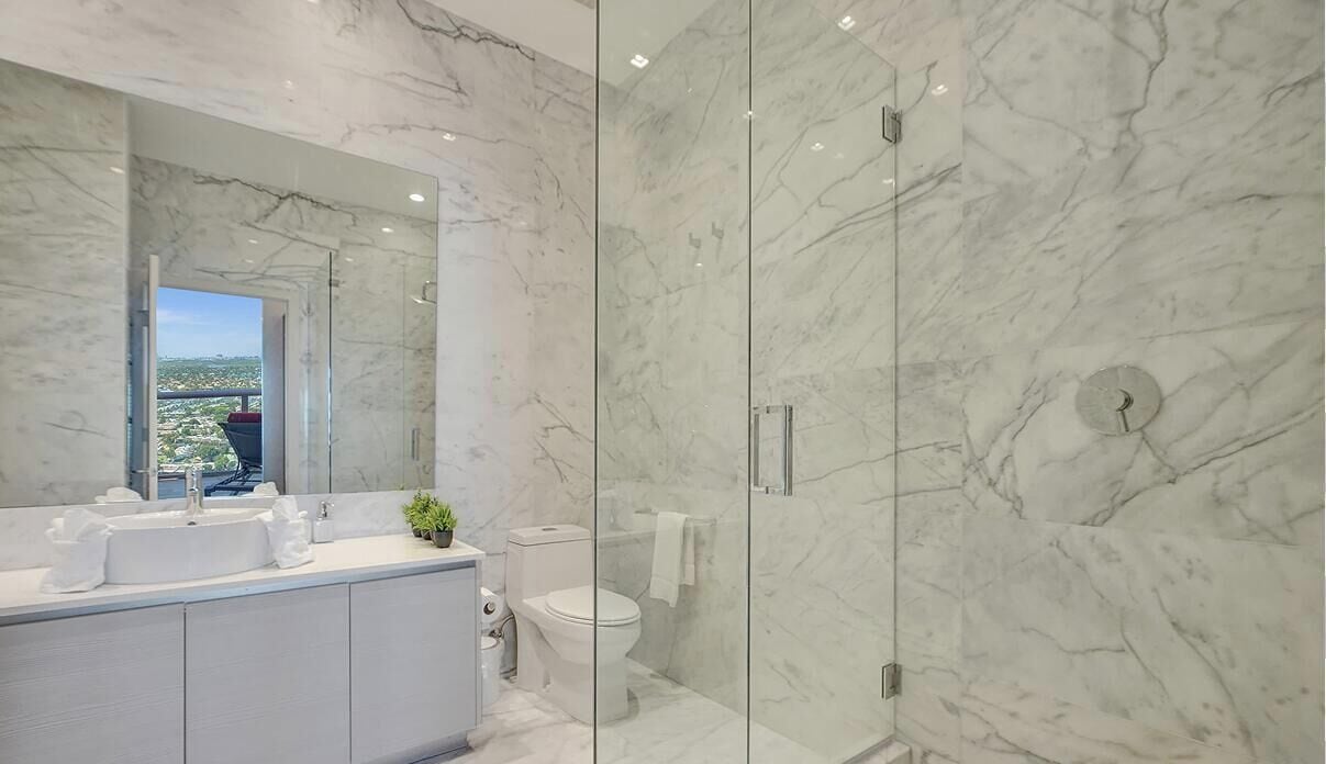 A modern bathroom with a marble vanity, a glass-enclosed shower, and a view of the city.