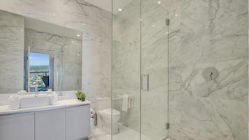 A modern bathroom with a marble vanity, a glass-enclosed shower, and a view of the city.