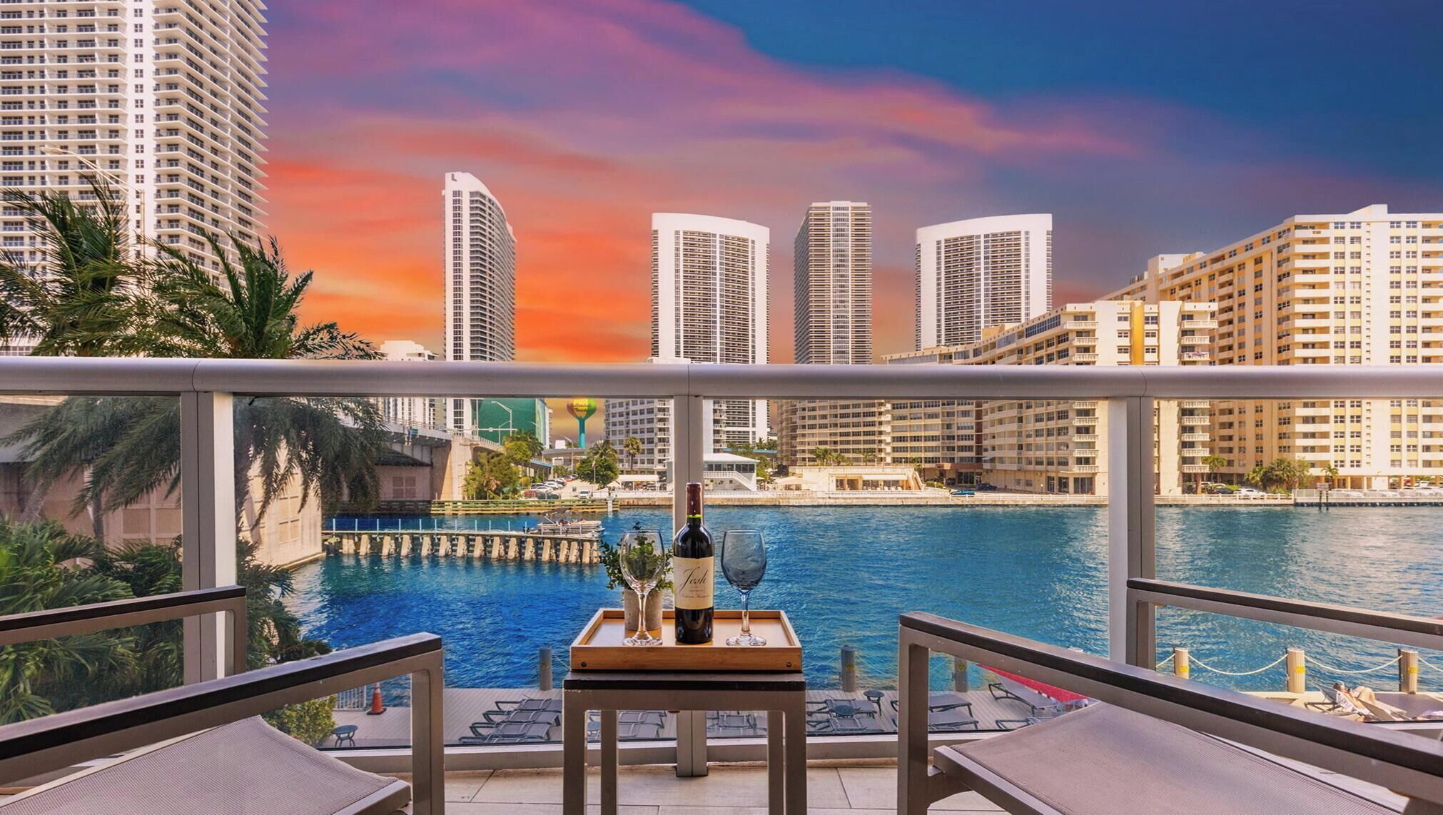 Un balcón con vistas al horizonte de una ciudad, una piscina y una botella de vino sobre una mesa.