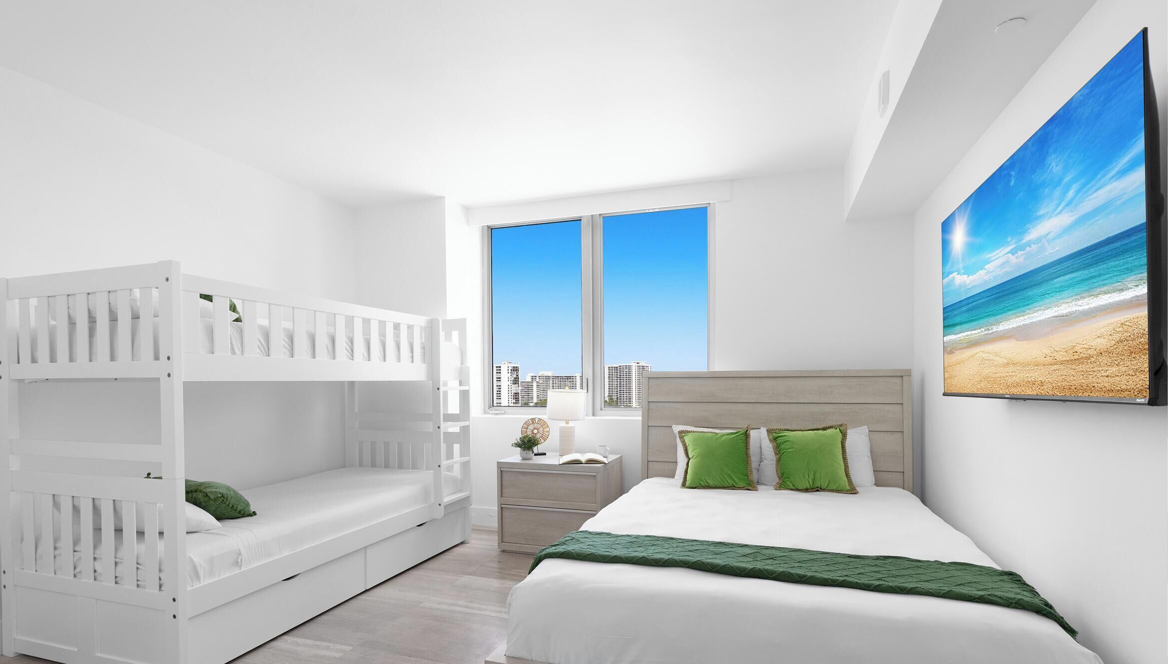 A bedroom with a bunk bed, a single bed, a nightstand, a lamp, and a large window with a city view.