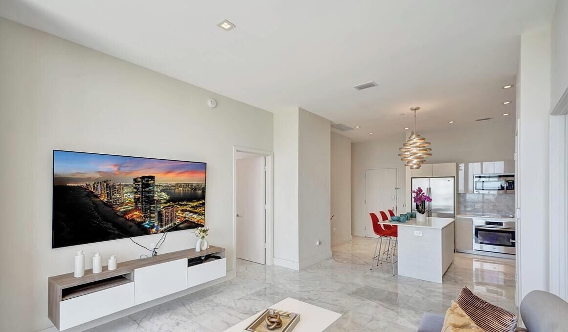 A modern living room with a large flat-screen TV, a kitchen area, and a dining space.
