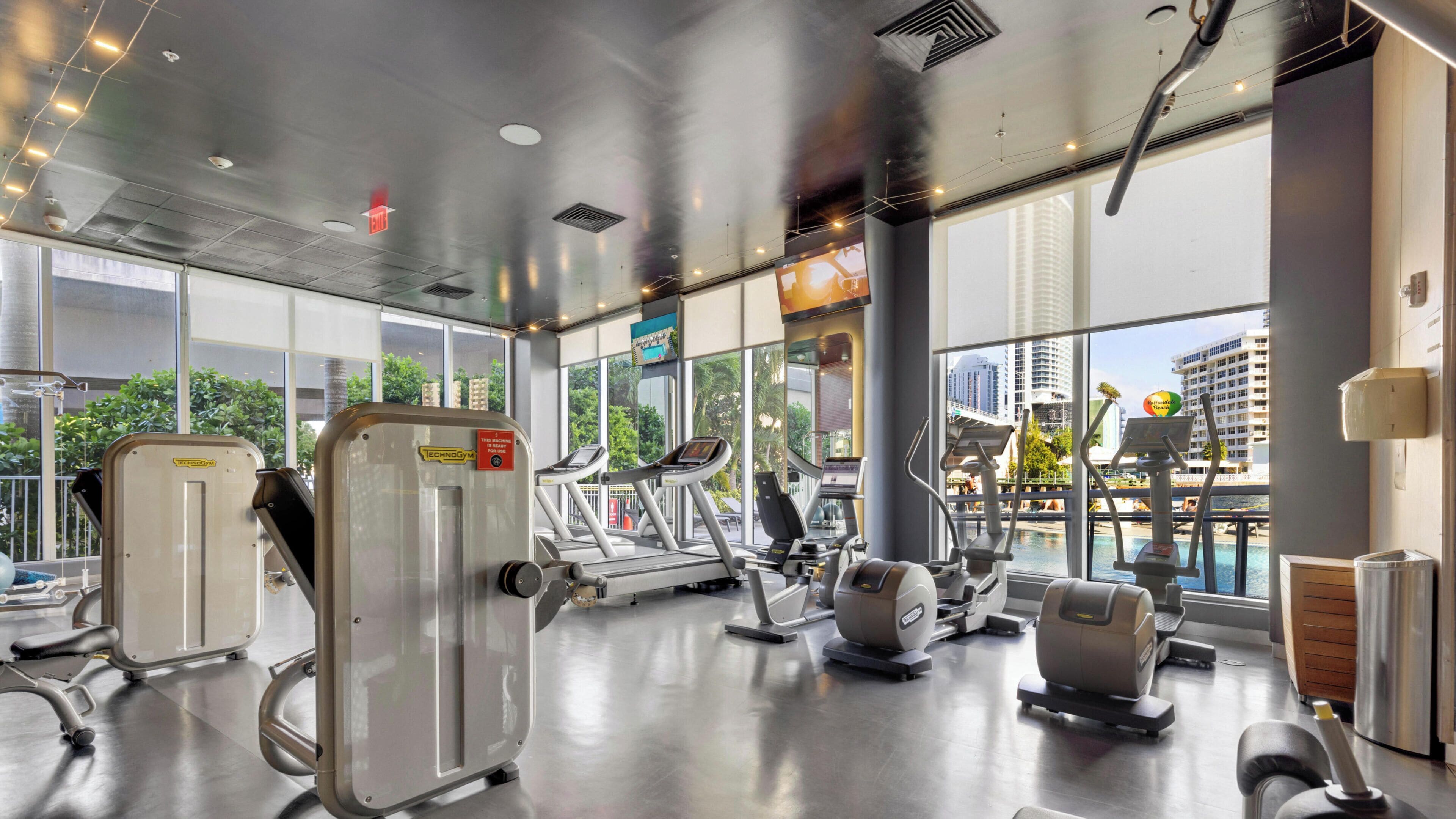A gym with cardio machines, weight equipment, and large windows offering city views.