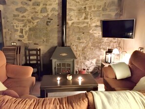 Ein gemütliches Wohnzimmer mit Steinwänden, Kamin, Flachbildfernseher und bequemen Sitzmöglichkeiten.
