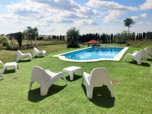 Ein Swimmingpool, umgeben von weißen Kunststoffliegen auf einer Rasenfläche mit Bäumen im Hintergrund.