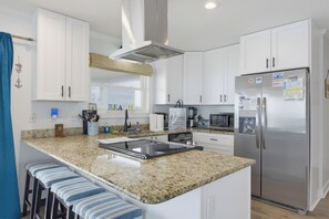 Una cocina moderna con armarios blancos, encimera de granito, refrigerador de acero inoxidable y horno microondas integrado.